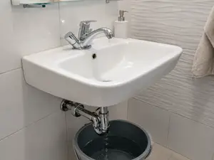 Cieknący syfon pod umywalką z podstawionym wiadrem w łazience