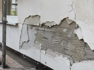 Uszkodzony tynk cienkowarstwowy na ociepleniu — odsłonięta siatka z włókna szklanego i klej zbrojący
